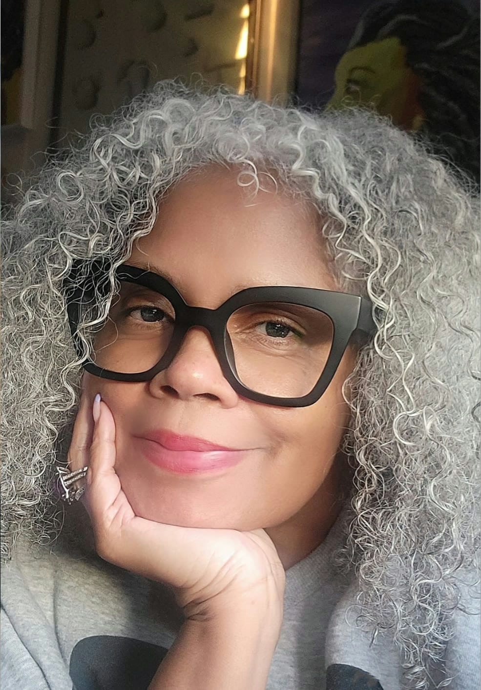 Kelly Walker Edwards smiling, chin resting on her hand, in dark-framed glasses