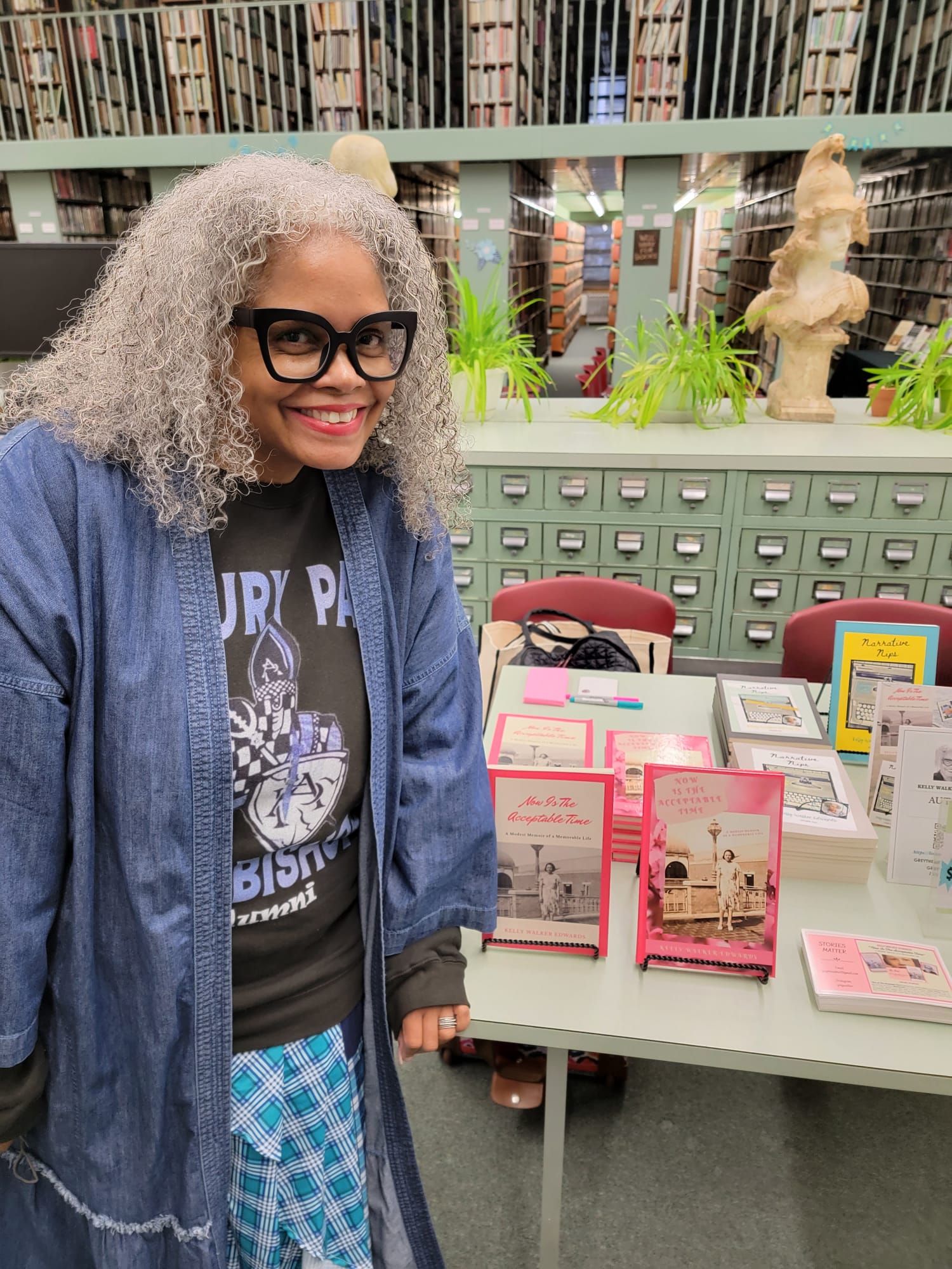 Kelly Walker Edwards beside a display table of her books, in front of the library's green wooden card catalogue drawers