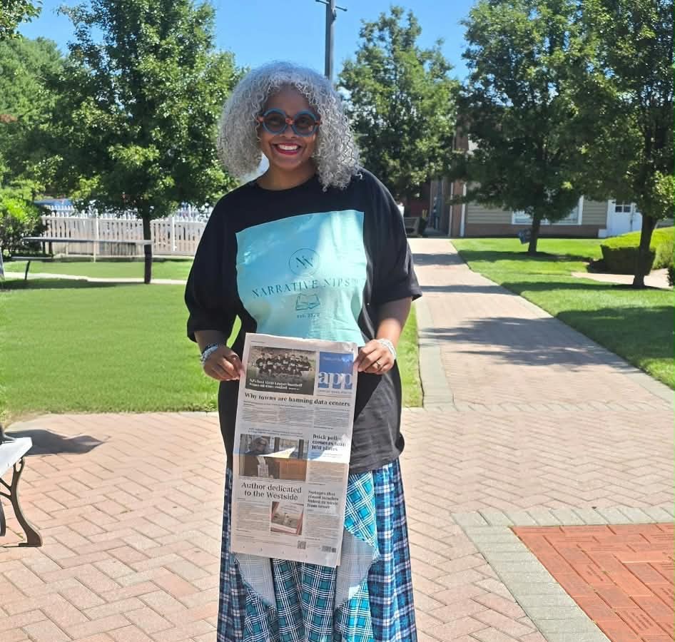 Kelly Walker Edwards outdoors, holding up the Asbury Park Press front page carrying her profile